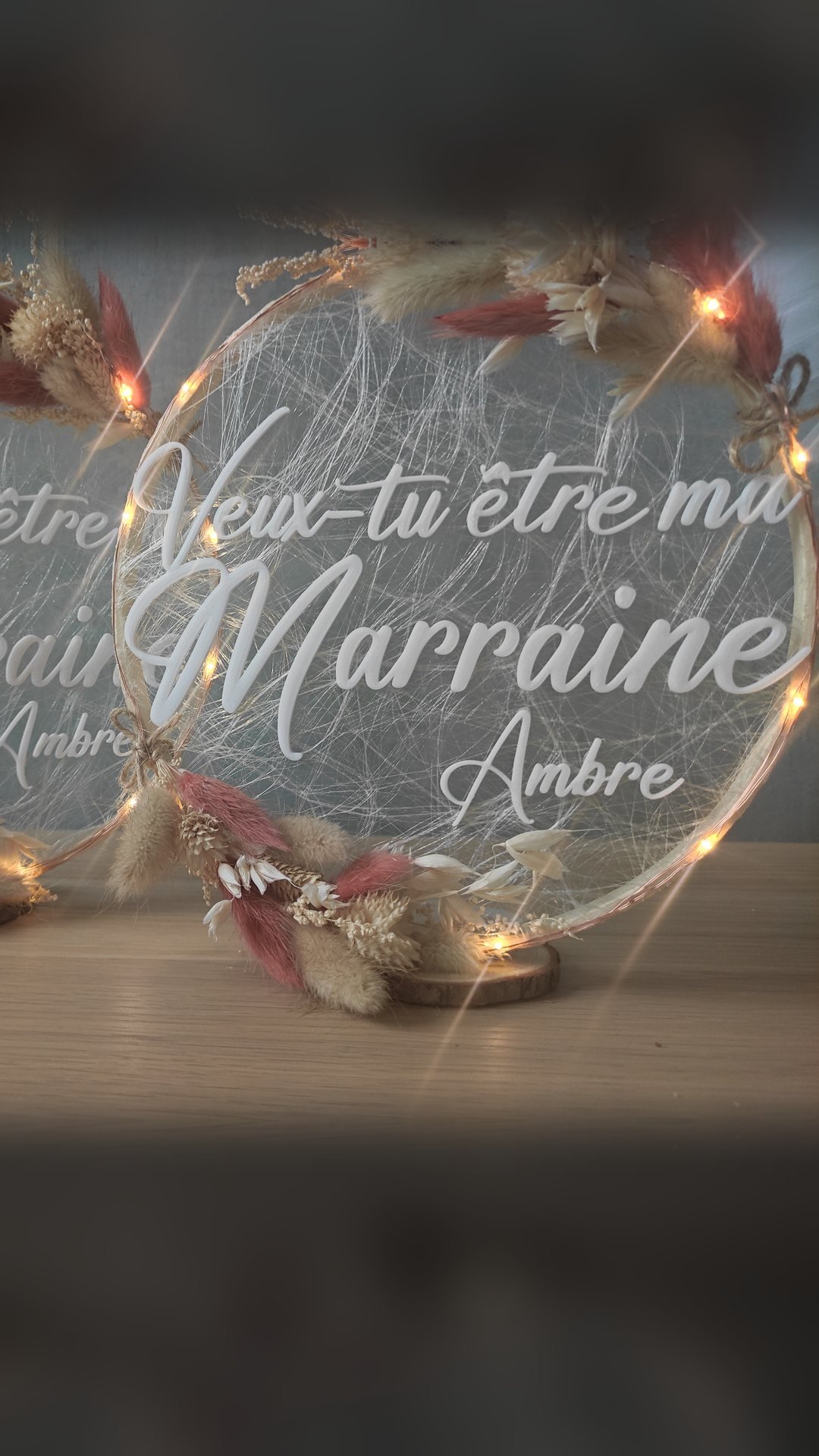 Deux cercles de fleurs séchées personnalisés, guirlandes LED allumées, portant la question « Veux-tu être ma marraine » et le prénom Ambre